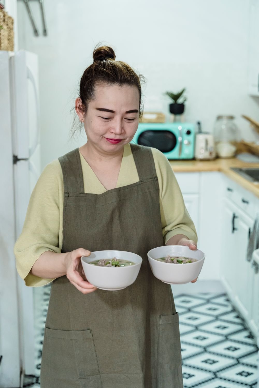 Mulher sorrindo enquanto serve duas tigelas de sopa na cozinha